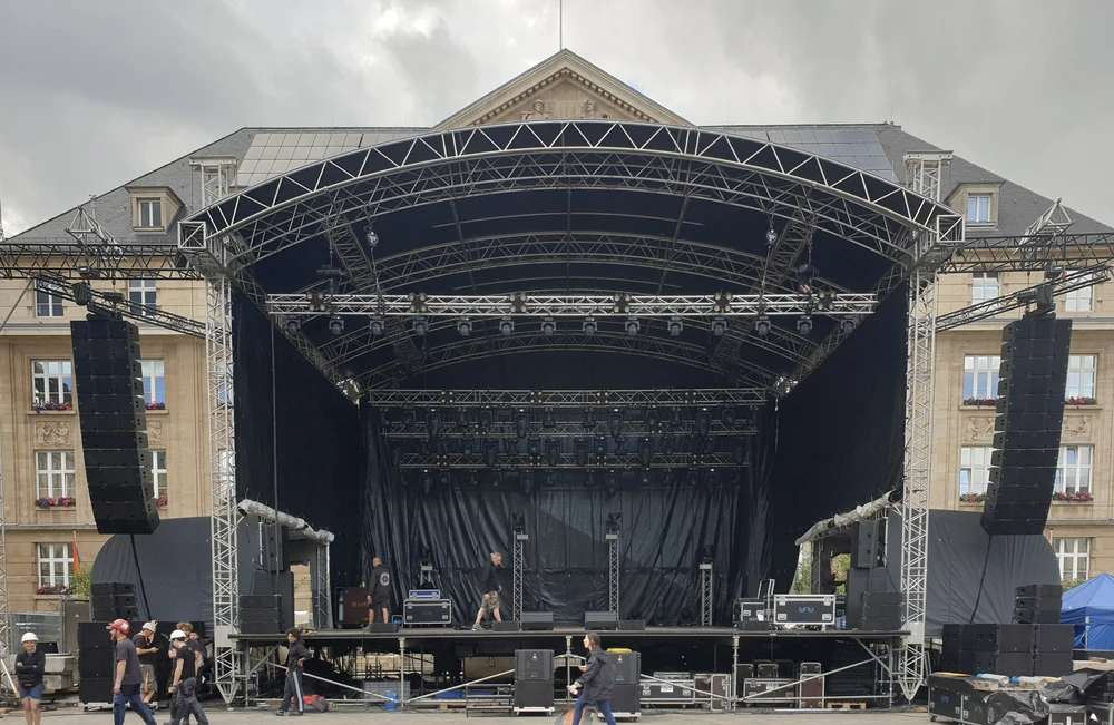 Scène extérieure avec une grande scène de concert temporaire montée sur une place urbaine