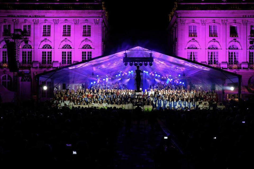 Scène extérieure de montage d'une scène de concert avec techniciens installant équipements audio et instruments