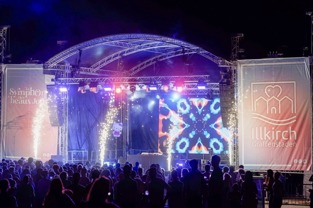 Scène extérieure de montage d'une scène de concert avec techniciens installant équipements audio et instruments