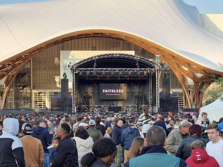 Scène extérieure de montage d'une scène de concert avec techniciens installant équipements audio et instruments