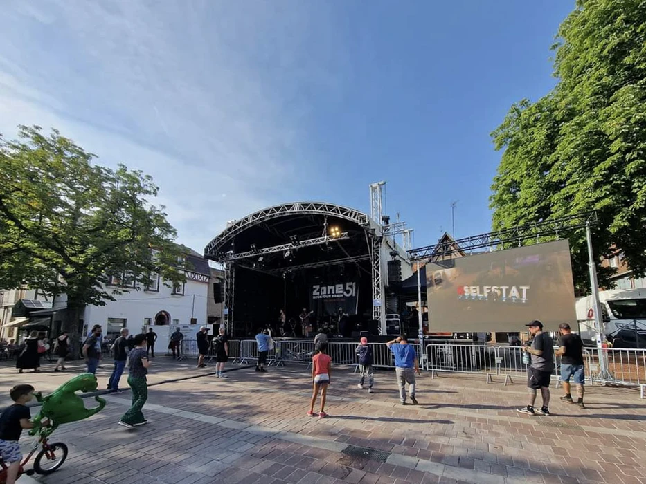 Scène extérieure de festival musical avec foule nombreuse devant une scène couverte