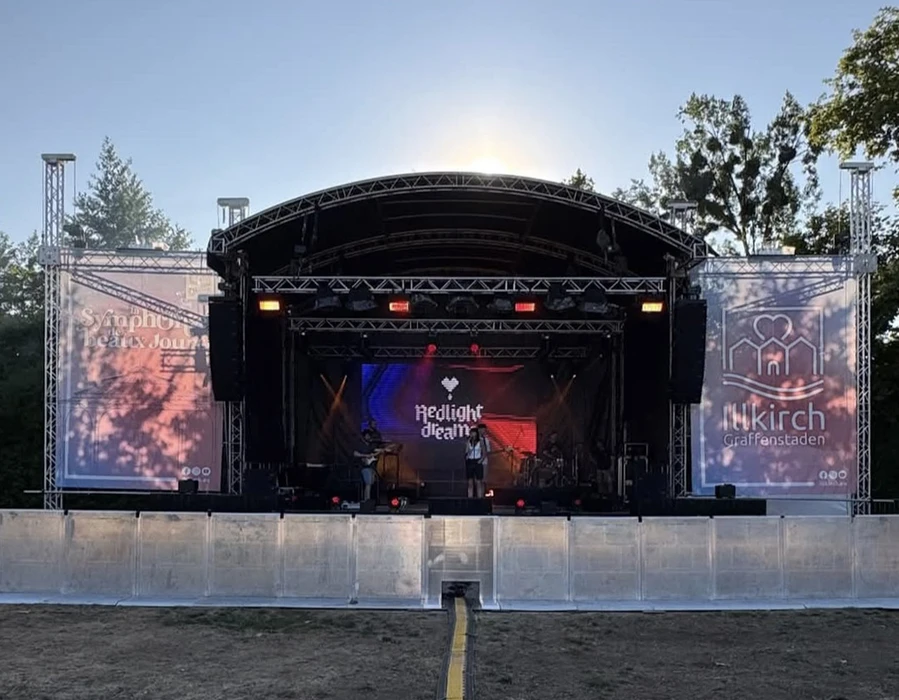Scène de concert en plein air avec grande scène couverte et foule nombreuse