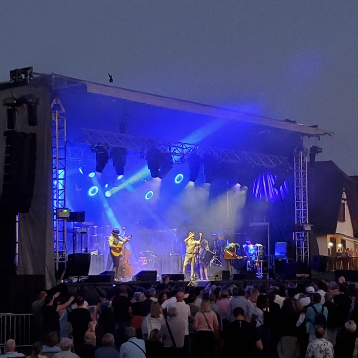 Scène extérieure de festival musical avec foule nombreuse devant une scène couverte