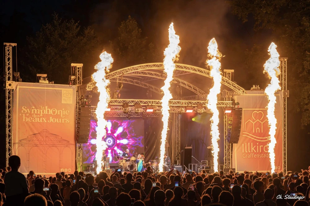 Scène extérieure de festival musical avec foule nombreuse devant une scène couverte
