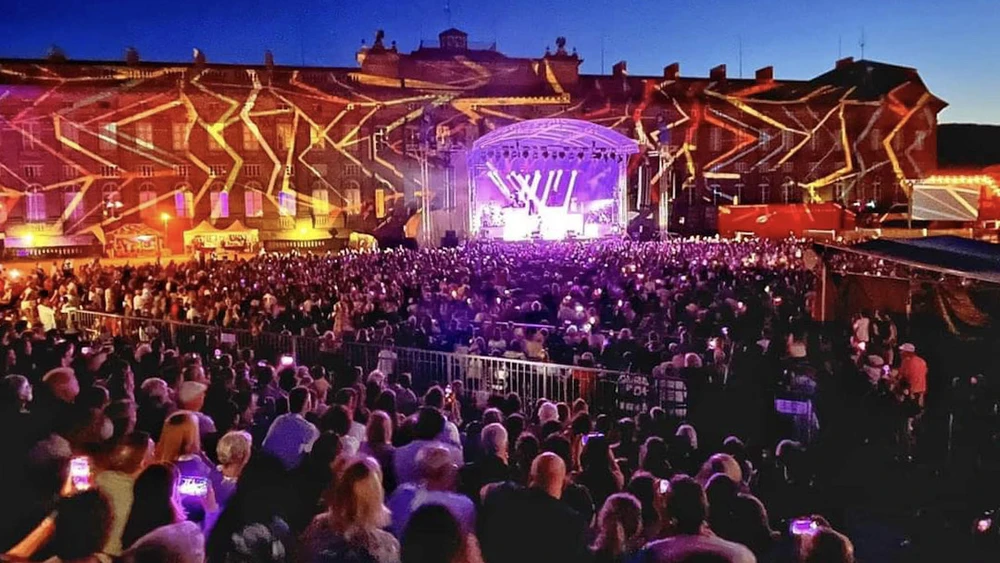 Scène extérieure de festival musical avec foule nombreuse devant une scène couverte
