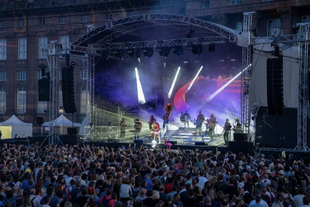Scène extérieure de festival musical avec foule nombreuse devant une scène couverte