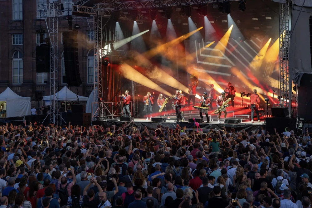 Scène extérieure de festival musical avec foule nombreuse devant une scène couverte
