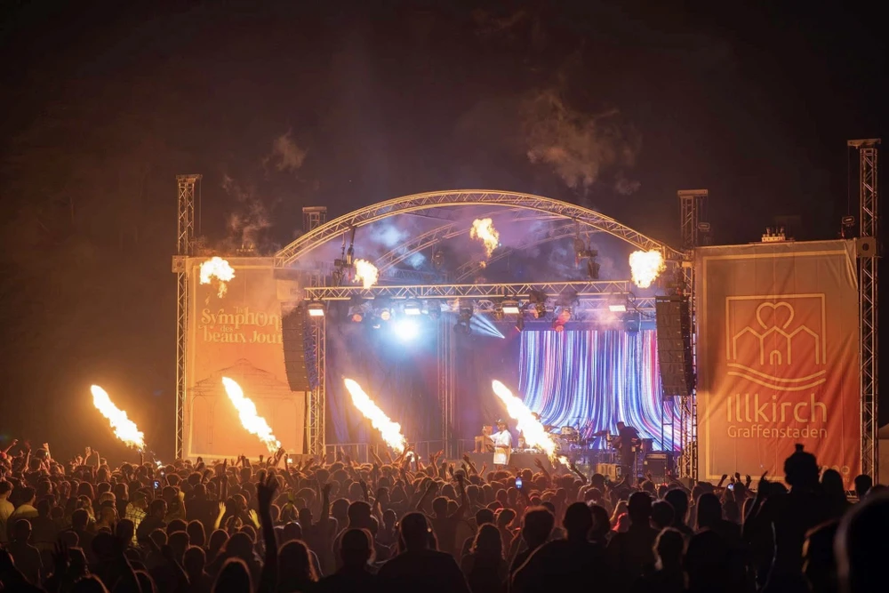 Scène extérieure de festival musical avec foule nombreuse devant une scène couverte